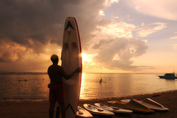 Silhouette image of tourists carrying surfboards against the backdrop of a sunrise on a paradise...