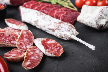Set of various spanish dry cured salami sausages slices and whole cuts on black textured background