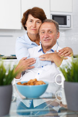 Portrait of happy mature couple hugging near kitchen table before drinking tea