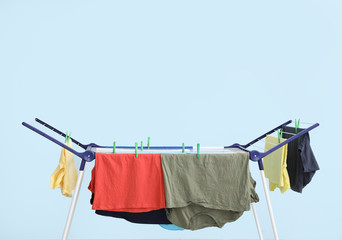 Clean clothes hanging on dryer against color background