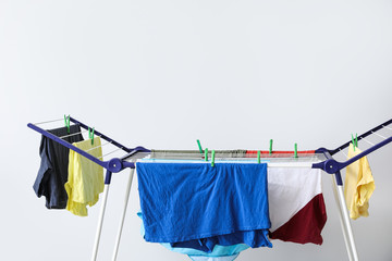 Clean clothes hanging on dryer against light background