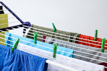 Clean clothes hanging on dryer against light background, closeup