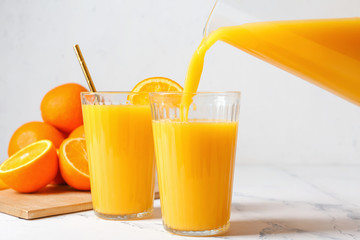 Pouring of fresh orange juice in glass on table