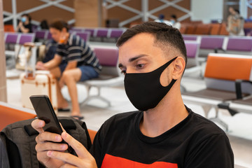A guy is waiting for a flight in a medical mask on his face in the airport lounge. Air travel during the coronavirus pandemic.