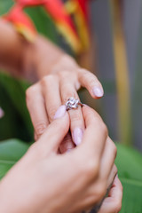 Close shot of womans hands wearing ring on finger on background of tropical leaf and red flowers. 