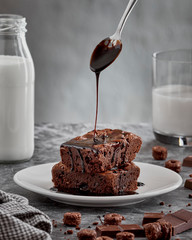 Chocolate brownie cake with chocolate syrup on bright background. Stack of brownie pieces  with pouring melted chocolate sauce. Close up view.