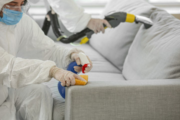 Workers in biohazard costume removing dirt from sofa in house