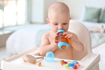Cute little baby drinking juice from bottle at home