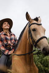 Fototapeta premium Young cow girl walking horse in green field. People and animal portrait. Horseback riding view. Active weekend