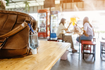 Mini portable alcohol gel bottle to kill Corona Virus(Covid-19) hang on a leather shoulder bag of a woman on table at cafeteria. New normal lifestyle.Selective focus on alcohol gel