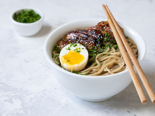 A bowl of ramen chicken soup with egg and sticks on a white background.