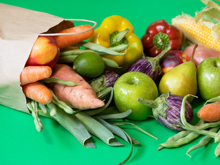 Vegan vegetarian food in paper bag vegetables and fruits on a green background. Grocery shopping food and zero waste concept.