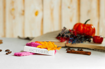 wooden cube with the inscription October in a cozy scarf with autumn leaves. old book, pumpkin and wildflowers on the background. autumn cozy picture