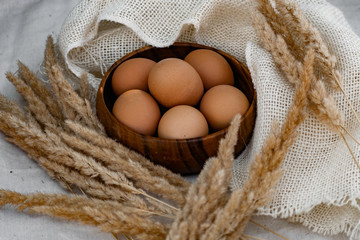 Chicken eggs in a deep wooden plate are laid out in a circle, next to dry twigs of Golden ears and...