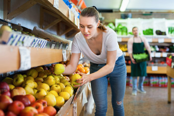 Fototapeta na wymiar Young positive woman customer choosing fresh apples on the supermarket.