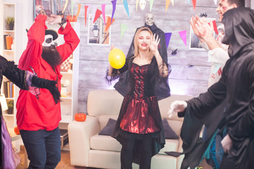 Cheerful vampire woman with bloody lips dancing with hands up at halloween celebration.