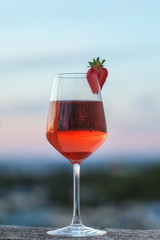 A glass of champagne against a blurred natural sky background. Glass of pink sparkling wine close-up. Festive evening. Soft focus, bottom view.