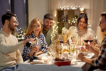holidays and celebration concept - happy friends having christmas dinner at home pouring non-alcoholic red wine