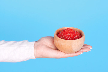 Salmon fish caviar, seafood on wooden jar in hand, isolated on blue background.