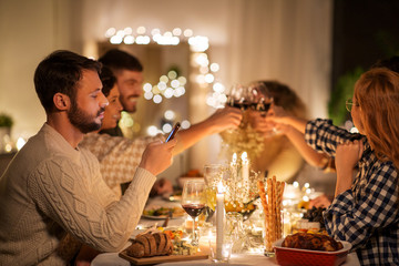 holidays and people concept - man with smartphone at dinner party with friends at home