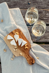 Two glasses of white wine and wooden plate with cheese and nuts during sunset time outside.
