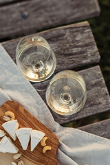 Fototapeta na wymiar Two glasses of white wine and wooden plate with cheese and nuts during sunset time outside.