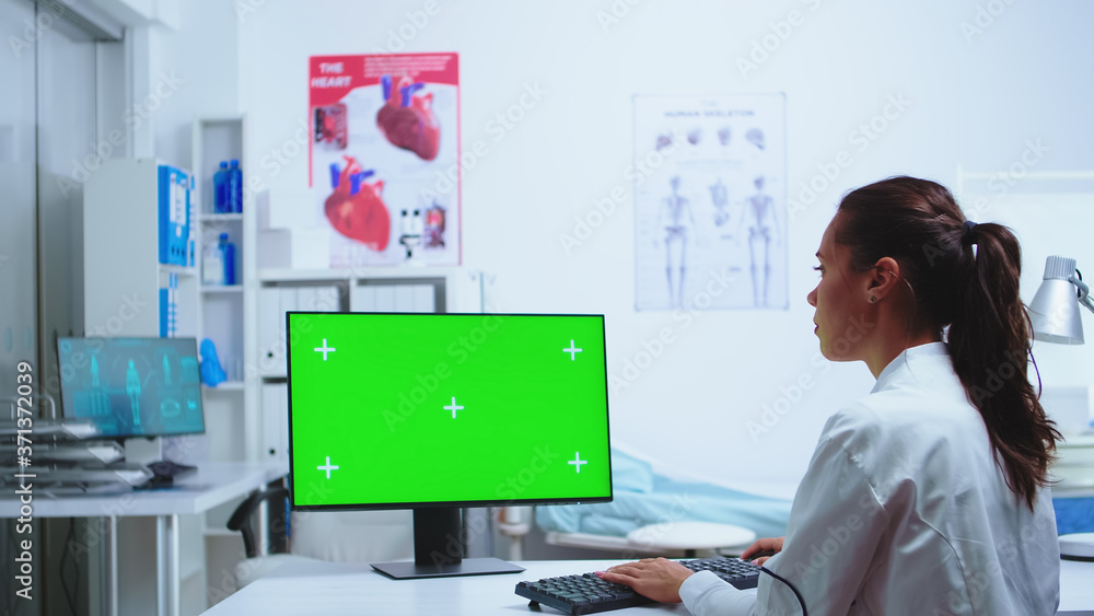 Poster medic writing diagnose on computer with green screen monitor while nurse is taking notes in the back