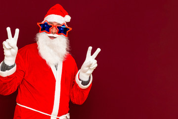 Close up joyful funny playful naughty santa showing peace victory signs, fooling around, in trendy specs, so confident.