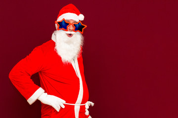 Santa claus look at camera red studio background with copy space for text He folded hands on the waist