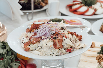 Chicken salad with baked bacon pieces on white plate close up. Festive table in the background