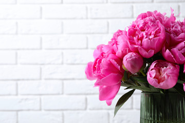 Bouquet of beautiful peonies in vase near white brick wall. Space for text