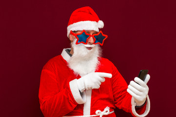 Portrait of satisfied santa claus use cell phone comment newyear posts reading news isolated over red background