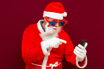 Portrait of satisfied santa claus use cell phone comment newyear posts reading news isolated over red background