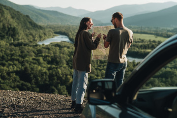 Traveler Couple on a Road Trip, Man and Woman Using Map on Journey Near Their Car Over Beautiful...
