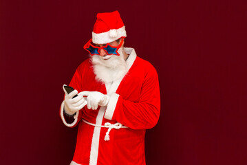 Portrait of satisfied santa claus use cell phone comment newyear posts reading news isolated over red background
