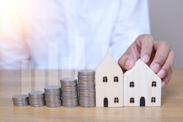 House Model, coins stacks and Graph background. property owner get money to home concept, small wooden house model on table with hand stacked coins.
