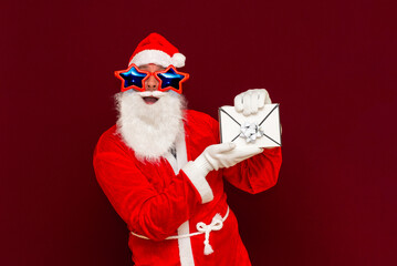 Fake Bearded man in Santa Claus hat holds gift letter envelope box. Ch hristmas gift. Christmas or New Year holidays.