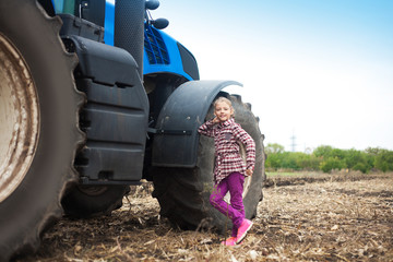 Cute girl near the modern tractor in the field.