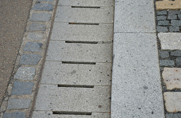 the edge of the road is drained by longitudinal channels of granite grids with gray slits at the...