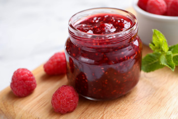 Delicious jam and fresh raspberries on wooden board, closeup