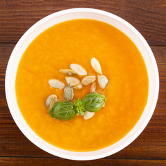 Pumpkin and carrot soup with cream and pumpkin seeds on wooden background with copy space. Top view