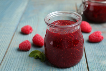 Delicious jam and fresh raspberries on light blue wooden table, closeup