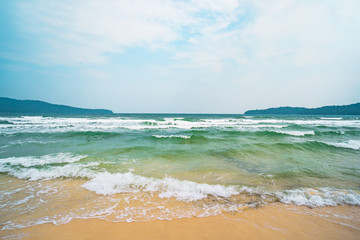 beach, white sand, blue ocean water and lush green tropical jungle, small green islands on horizon.