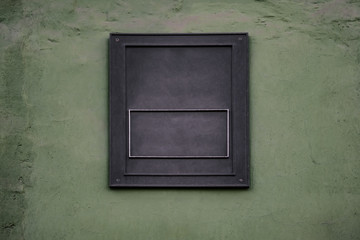 Obraz na płótnie Canvas Empty metal plaque template on green wall. Background with copy space of rough rectangular blank sign with four screws in the corners
