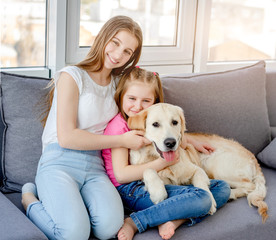 Smiling girls cuddling lovely dog in light room