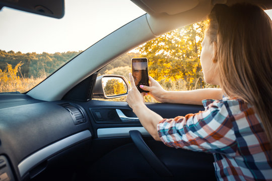 young woman makes selfie on the phone from the car window. travel in nature