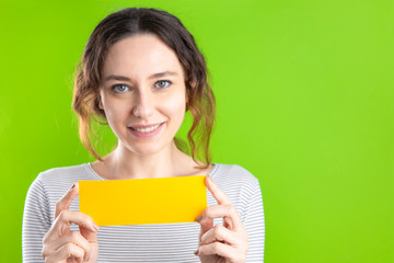 Young woman holding a yellow blank placard against a green background