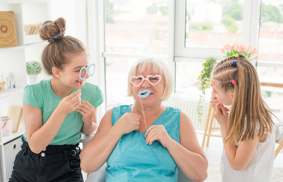 Smiling girls and senior woman with paper glasses and lips in light room