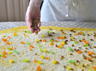 woman's hand sprinkles the dough with candied fruits and raisins