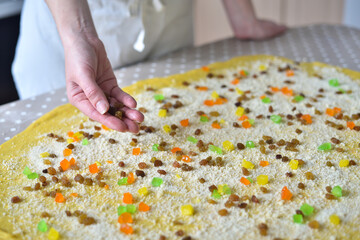 woman's hand sprinkles the dough with candied fruits and raisins